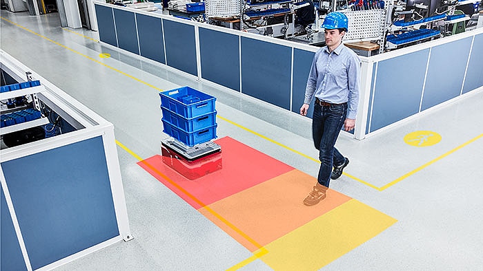 A man crosses the path of an automated guided vehicle in a production facility and is reliably detected.