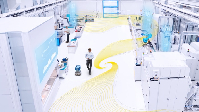 A man with a tablet is walking about in a production facility equipped with robots and mobile platforms. A yellow graphic element moves around the production area and symbolizes safe productivity.