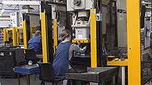 Two workers working at manual insertion presses.